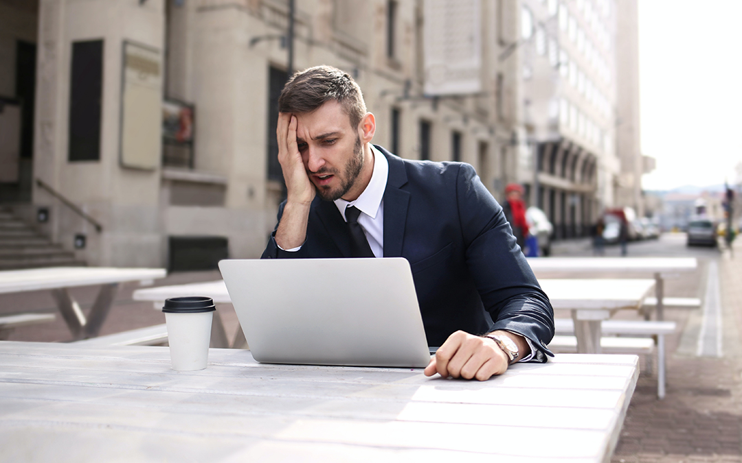 Corporate Stress Management, image of a man in a business suit sitting with his laptop stressed.